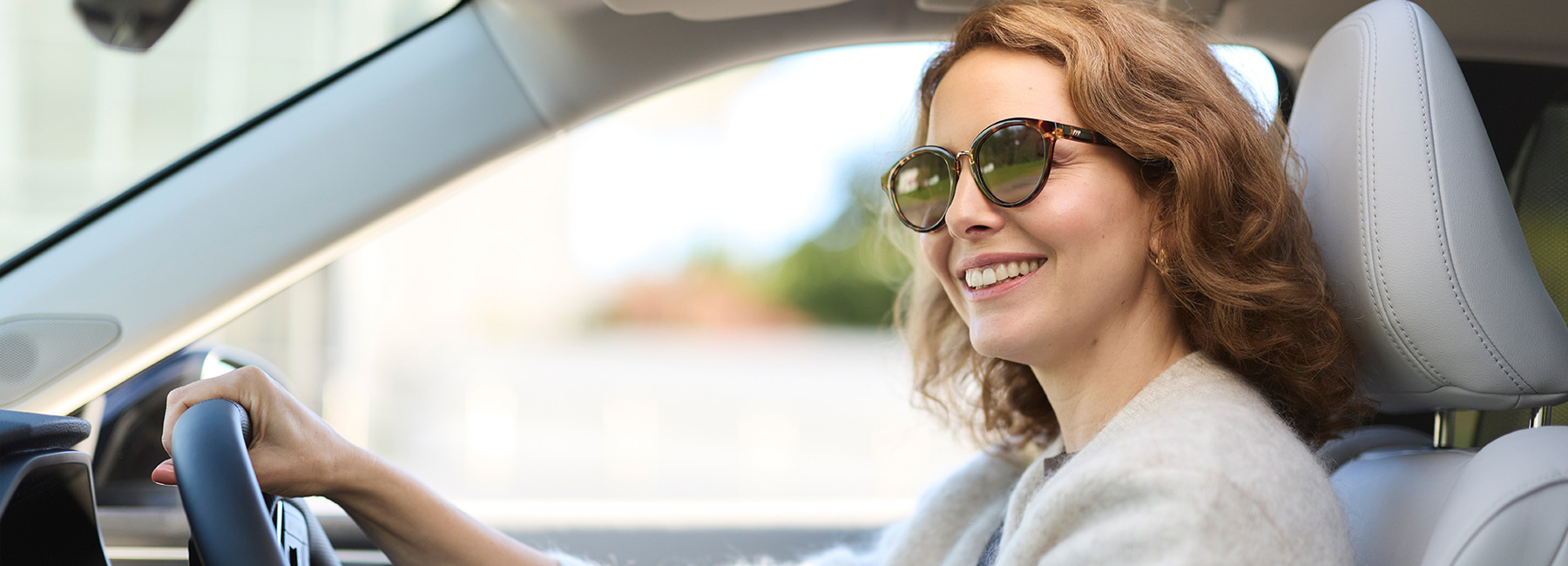 A woman with curly brown hair and sunglasses driving a Mitsubishi SUV