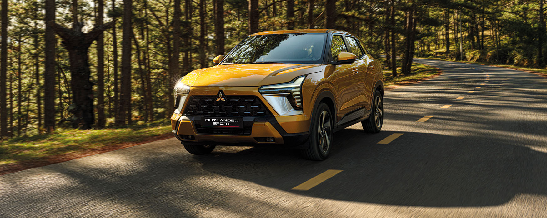 A yellow Outlander Sport driving on a forest road